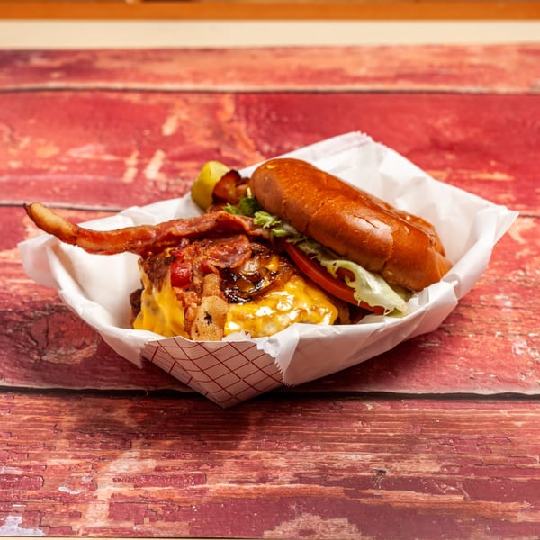 A Railroad Cafe burger with bacon, cheese, lettuce, tomato, and caramelized onions in a paper tray.