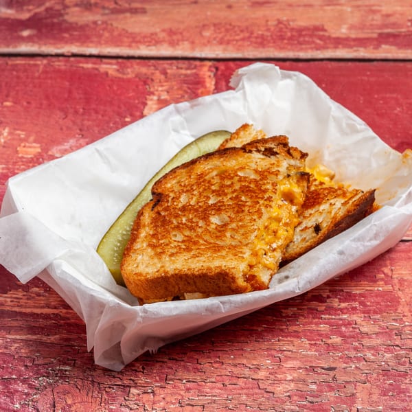 Grilled cheese sandwich with a pickle spear in a paper-lined basket on a rustic red wooden table.